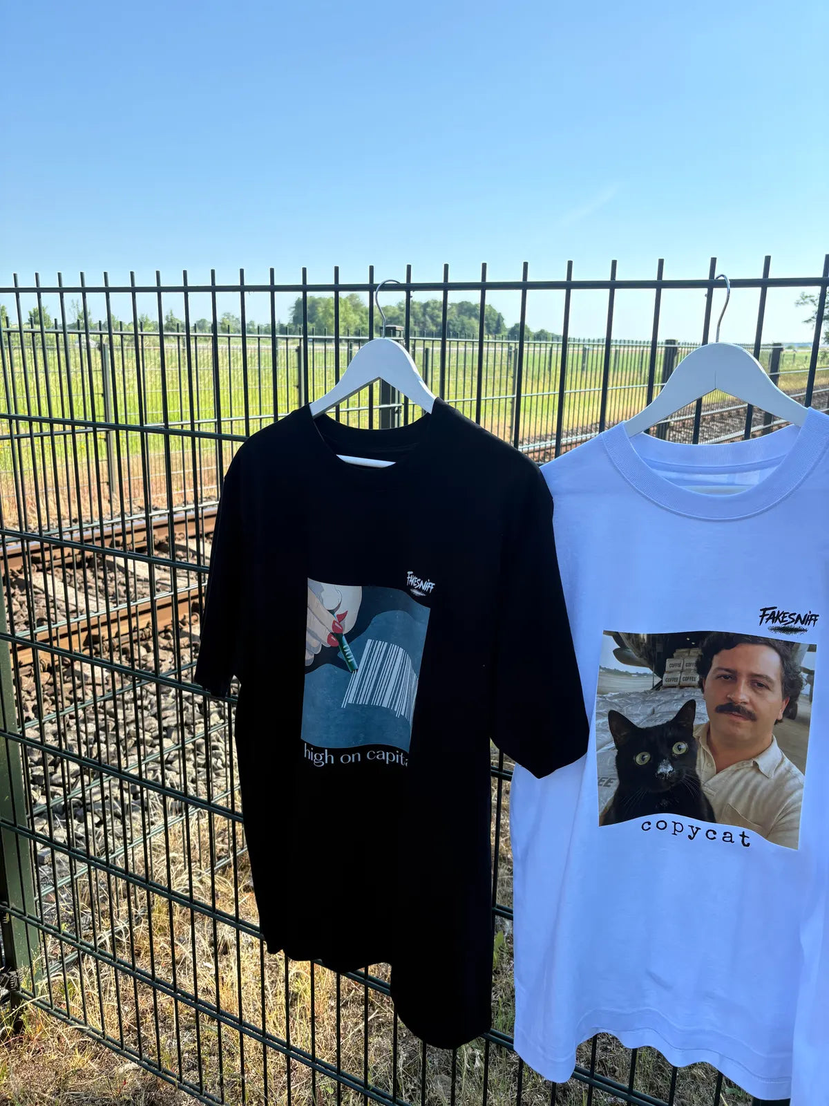 Twee shirts op hangers aan een hek, met het spoor erachter.