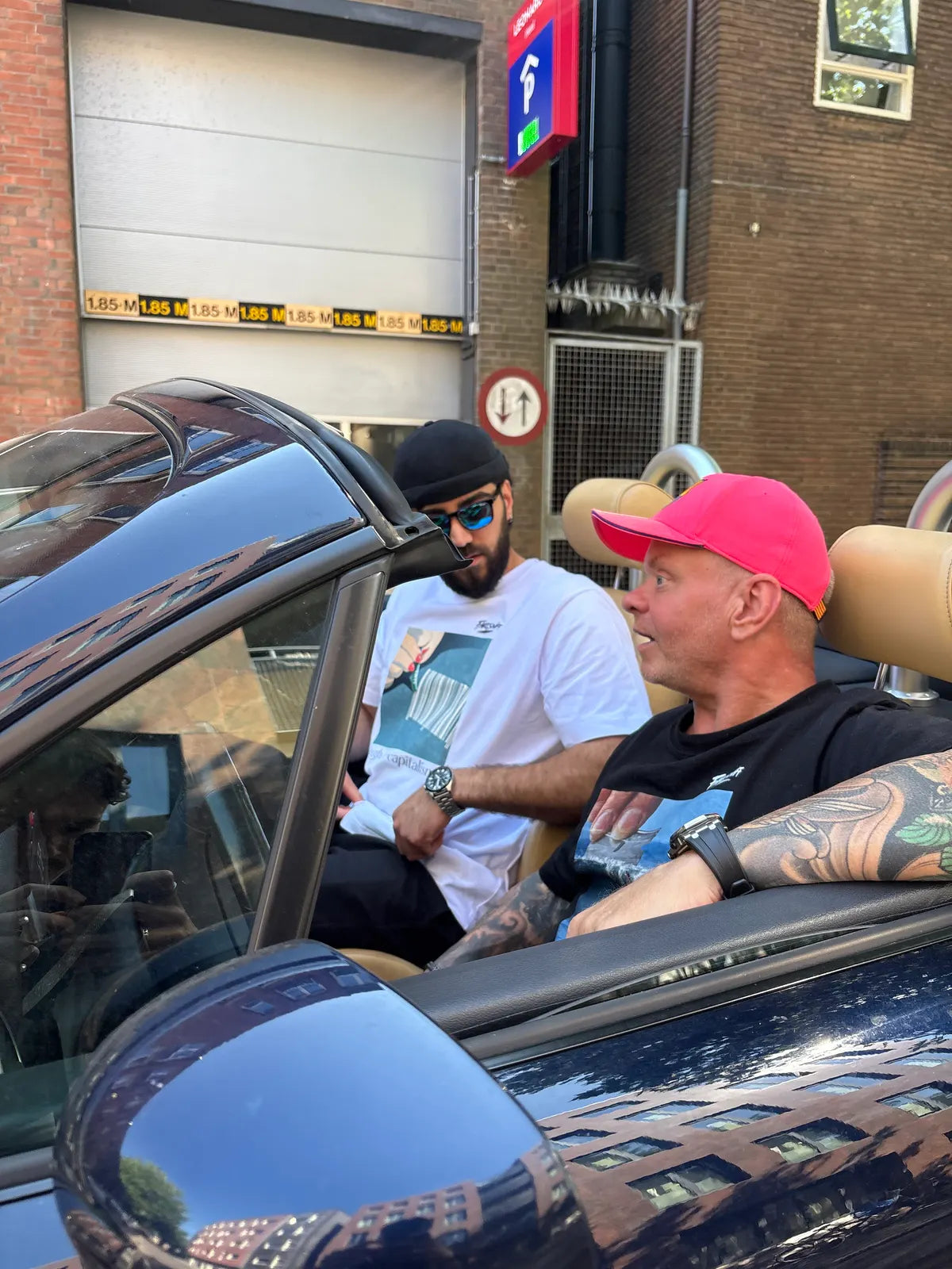 Twee mannen in een open auto voor een parkeergarage.