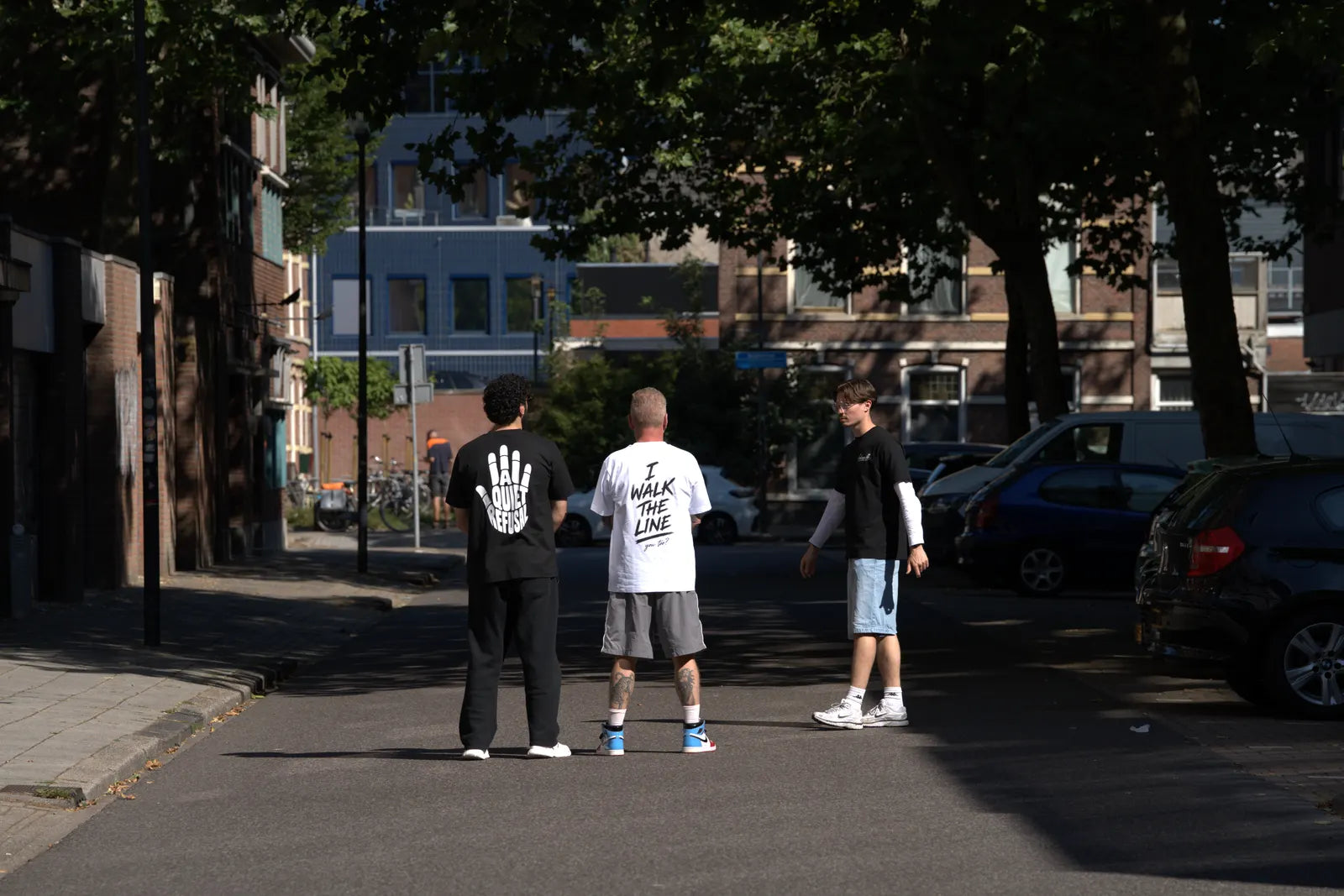 Drie mannen staan met hun rug naar de camera op straat.