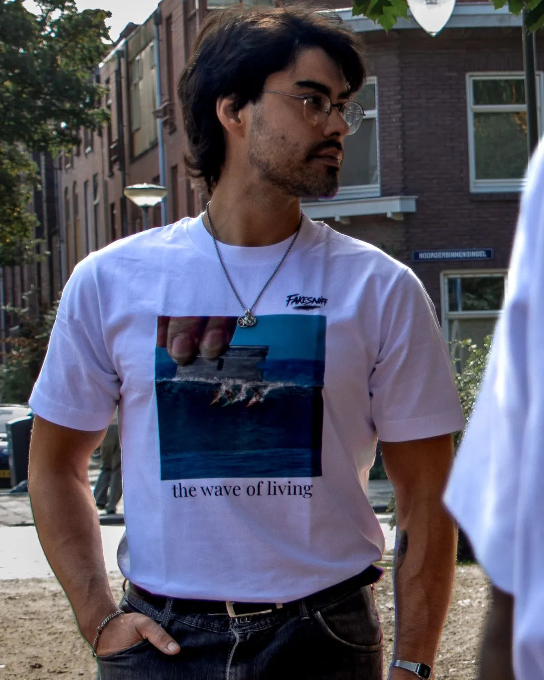 Een man met bril op straat, met huizen erachter.