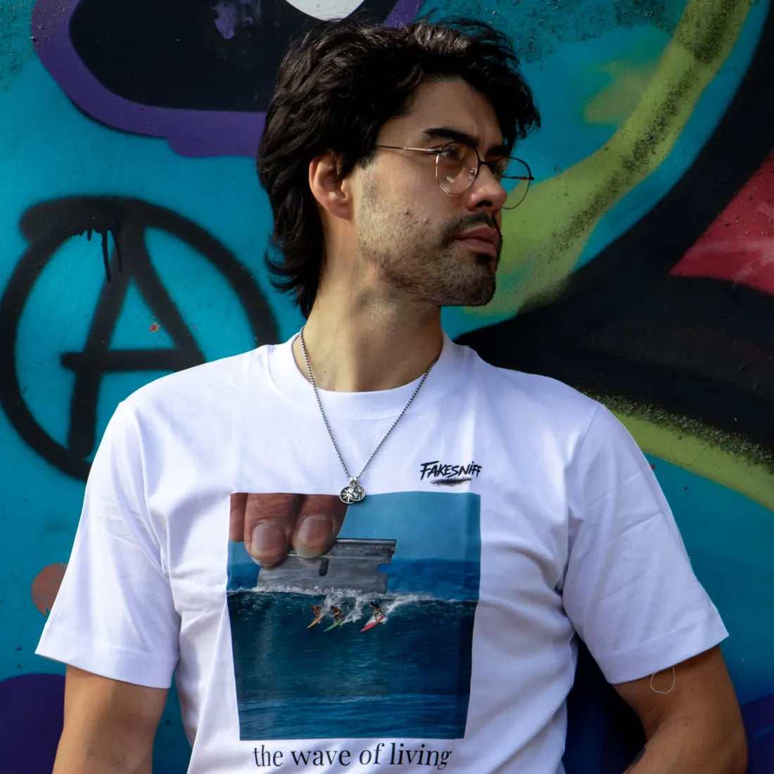 A man wearing glasses leans against a graffiti wall.
